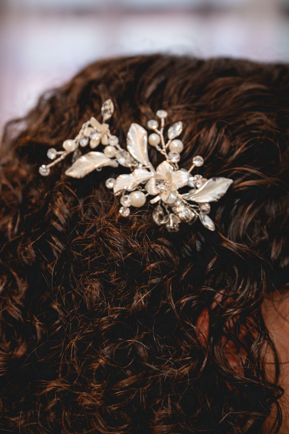 Silver floral hair comb with pearls and crystals adorning dark curly hair, perfect for bridal or formal occasions.