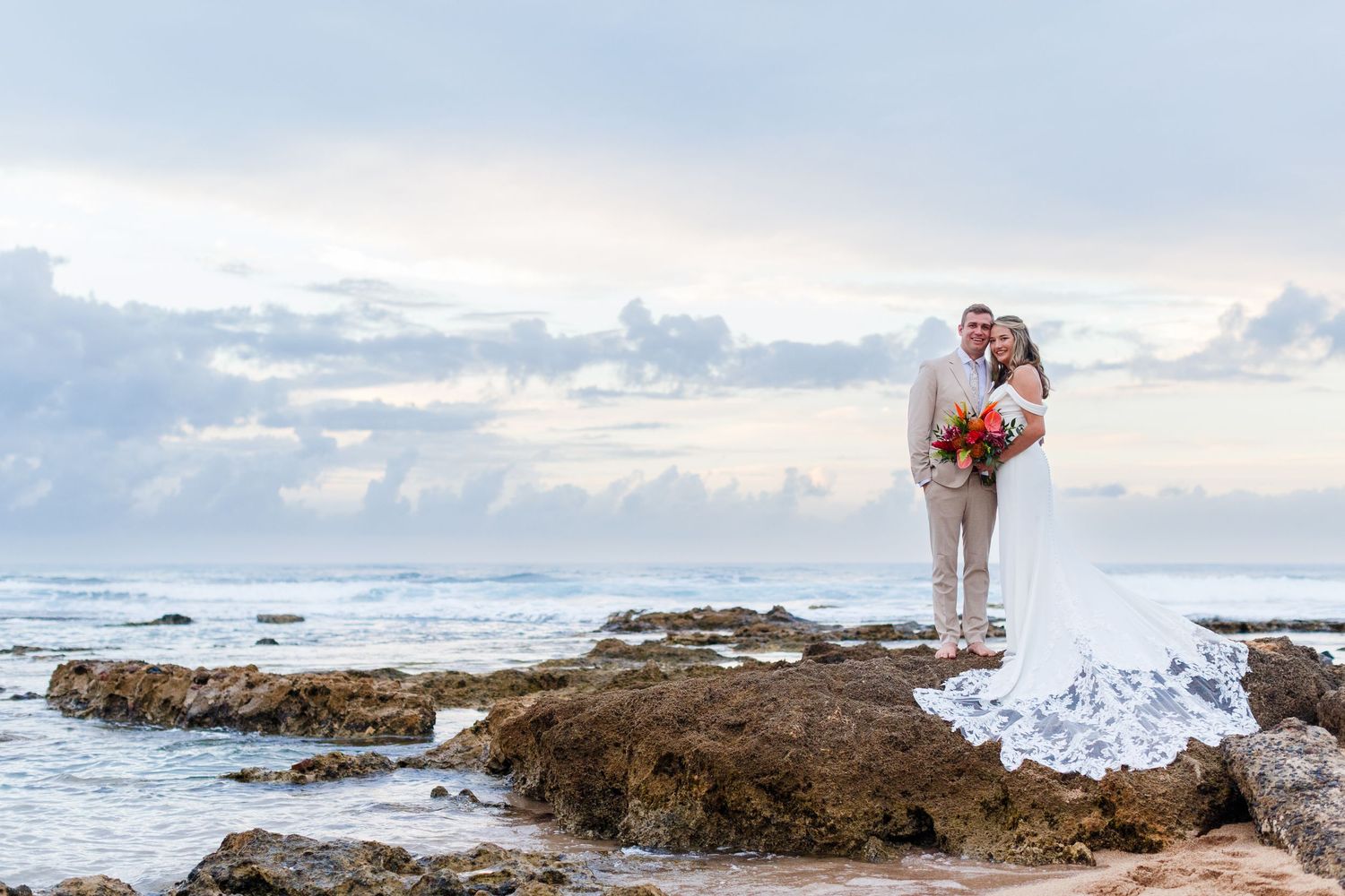 Wedding portrait. Bride and groom standing on rocks at the water's edge at the beach. Balneario del Escambrón, Old San Juan, Puerto Rico.