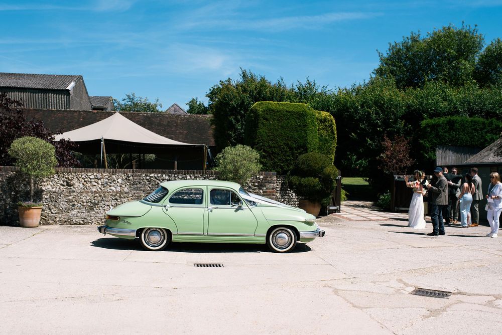 Vintage mint green classic car parked outside a rustic stone wedding venue on a sunny day.
