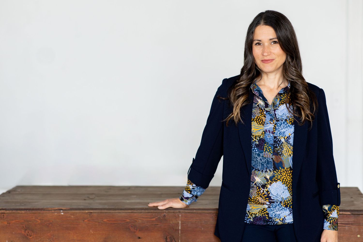 Professional portrait featuring a navy blazer and floral blouse against a minimalist white background.