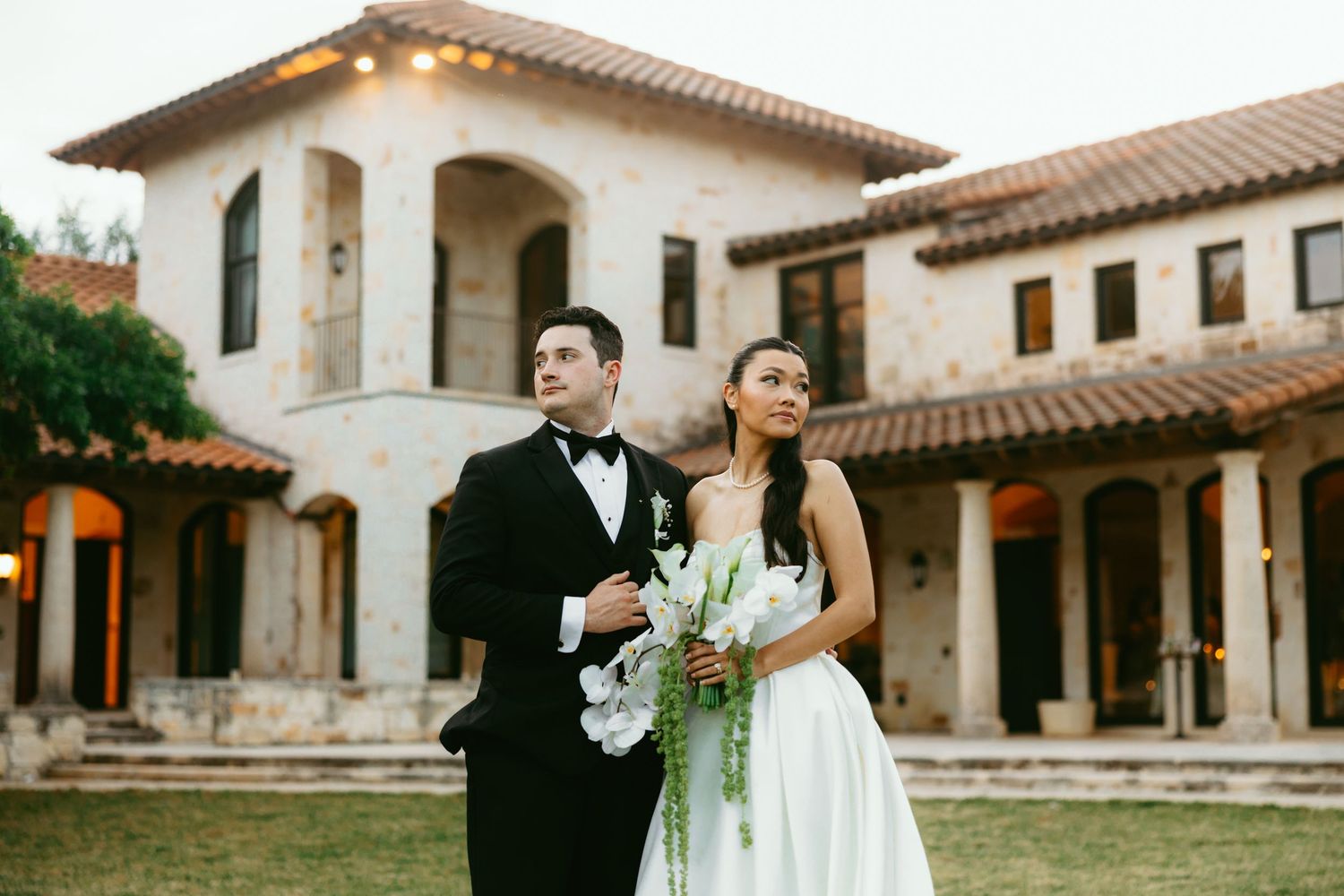 Bride and groom share romantic dip kiss at outdoor wedding ceremony with white floral arrangements and serene pond backdrop.