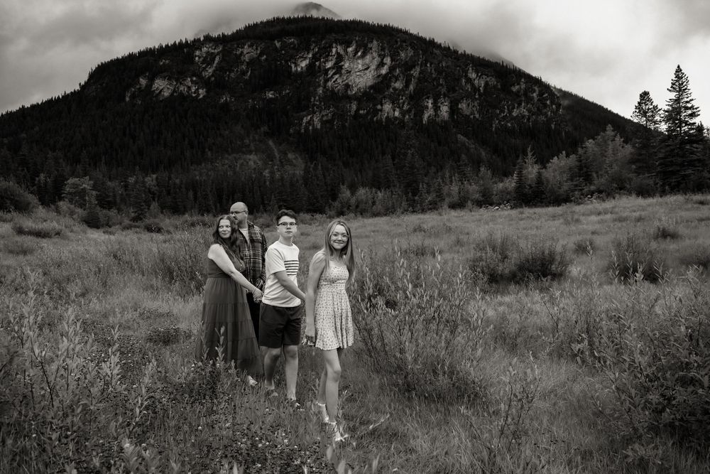 Black and white family photo of four people standing in a mountain meadow with a forested peak in the background.