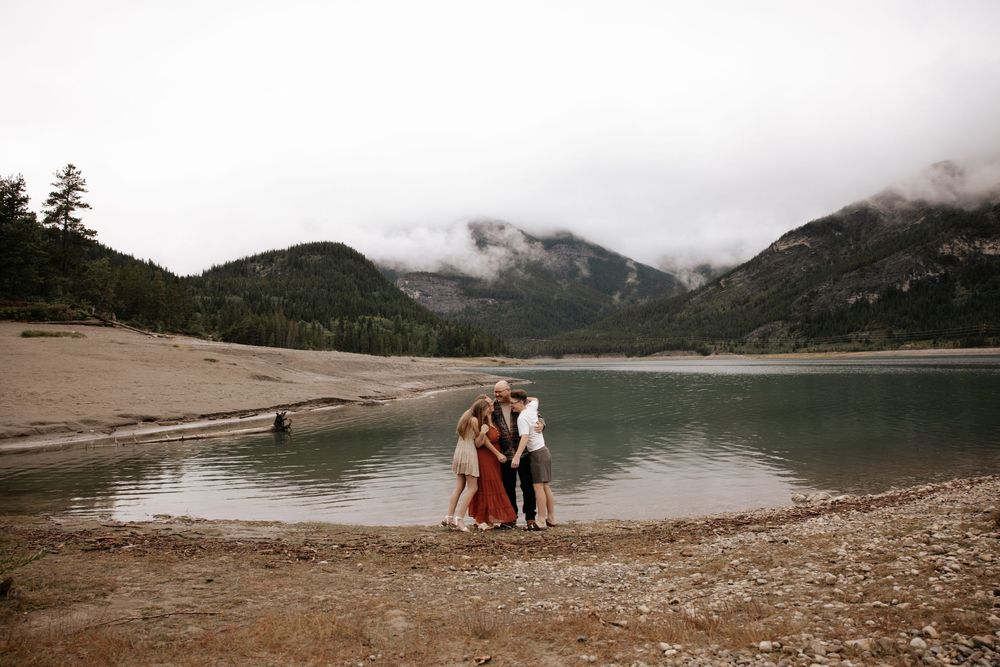 A couple and friends pose by a serene mountain lake with misty peaks and forested hills in the background.