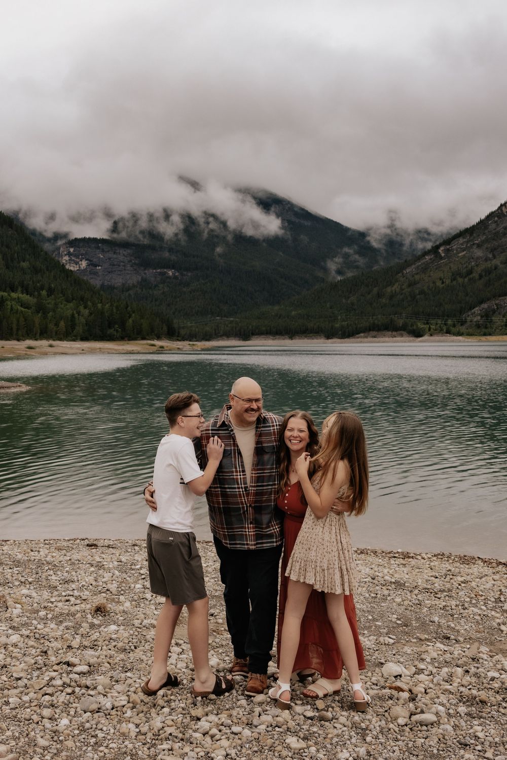 Family of four laughing together on rocky shore of mountain barrier lake alberta