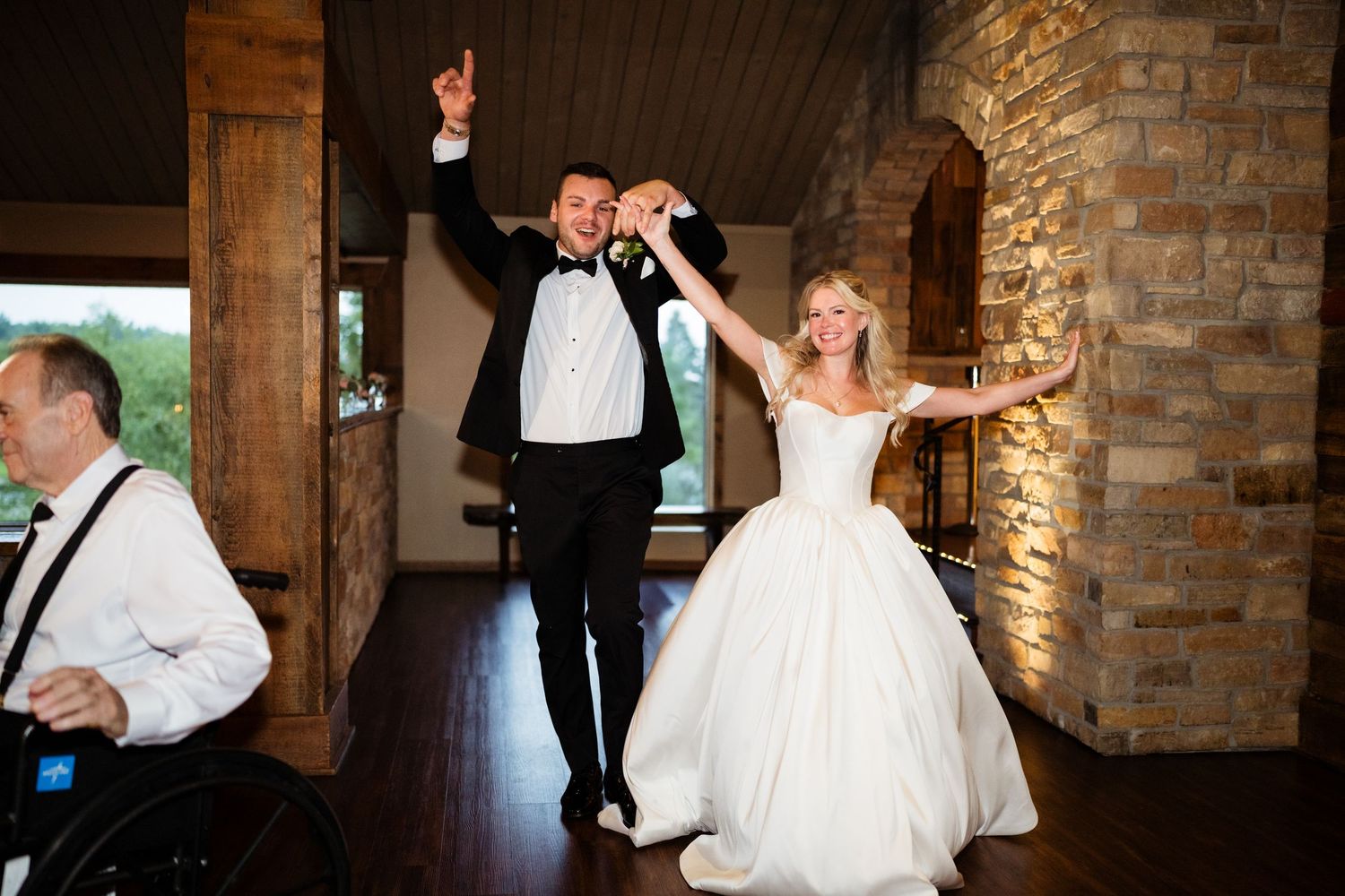 Bride and groom make grand entrance at wedding reception, holding hands and celebrating in elegant stone venue.