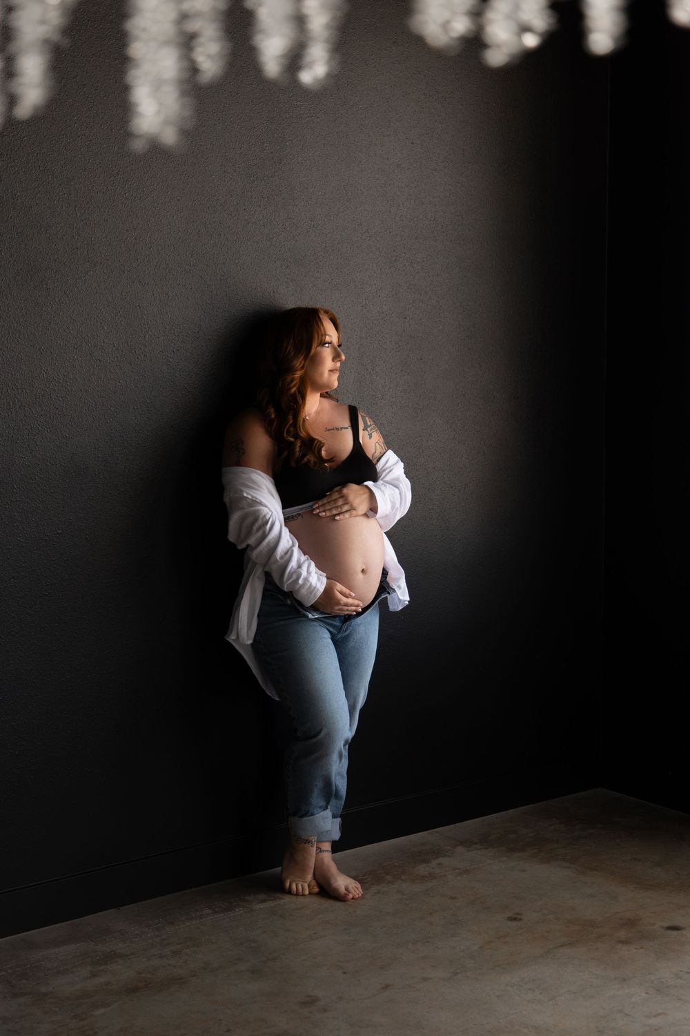 Moody maternity boudoir portrait of a pregnant woman posing in a dark studio