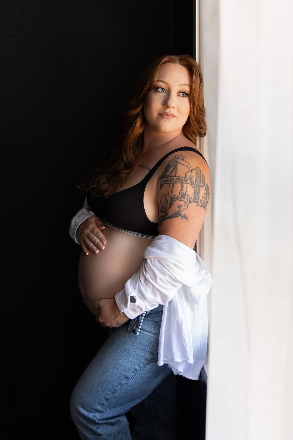 Pregnant woman posing in black lingerie during a dramatic maternity boudoir session