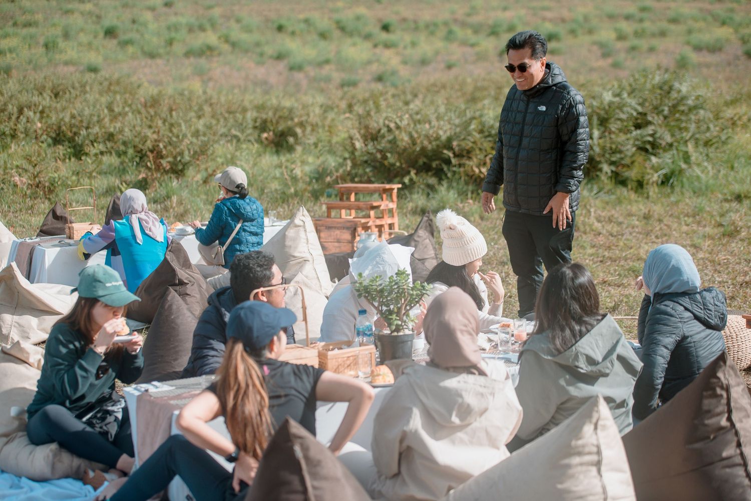 Group of people relaxing on bean bag chairs outdoors in a field during a casual picnic gathering.
