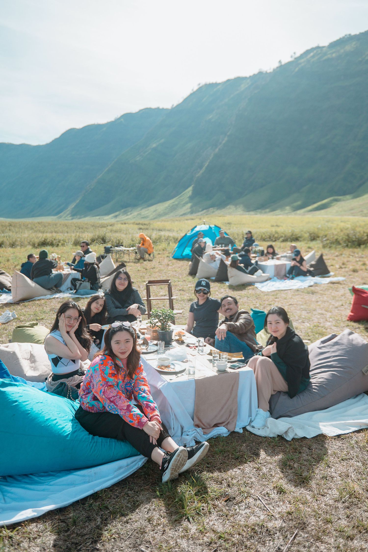 Group of friends enjoying an outdoor picnic on bean bags with mountain backdrop on a sunny day.