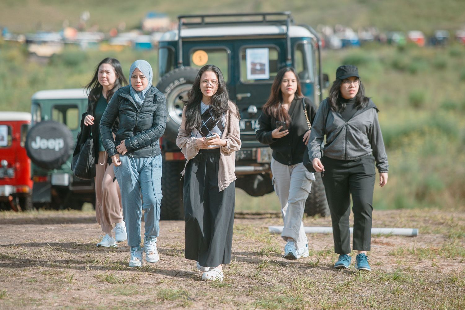 Group of women walking outdoors near Jeep vehicles at an off-road event in a scenic green landscape.