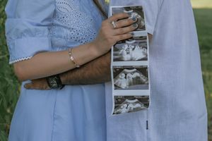 Couple holding ultrasound photos outdoors, wearing matching blue outfits, announcing pregnancy with sonogram strip.
