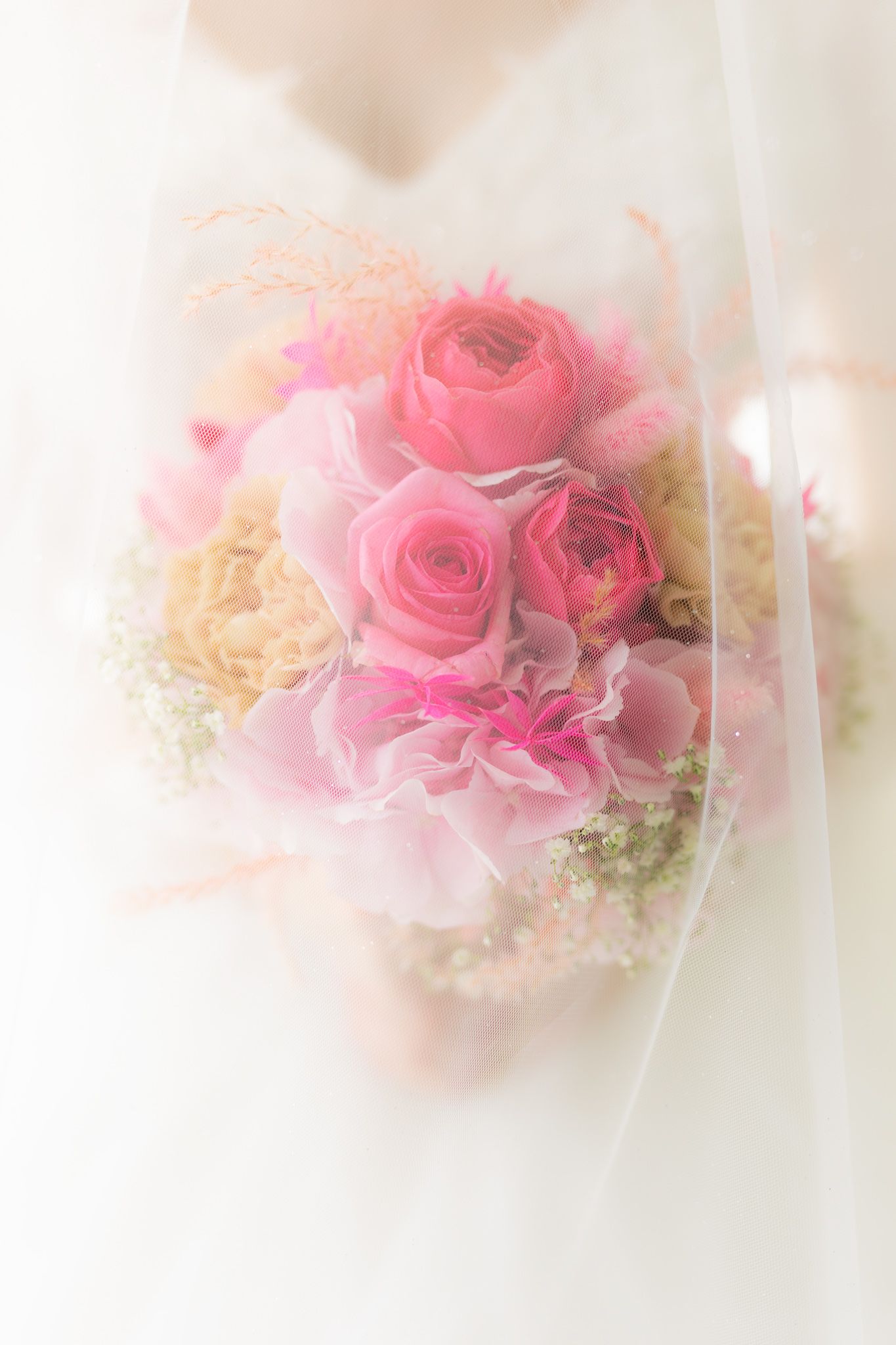Bride holding a soft pink wedding bouquet with roses and ranunculus, draped with a sheer veil.