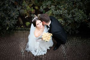 Bride and groom sharing a kiss captured from above, bride holding yellow bouquet in white gown with veil on cobblestone path.