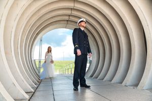 Bride and groom posing in a curved white tunnel archway, with blue sky visible in the background.