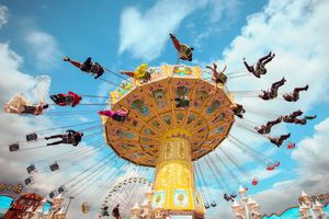 Colorful carnival swing ride with excited riders soaring through the air against a bright blue sky at a festive amusement park.