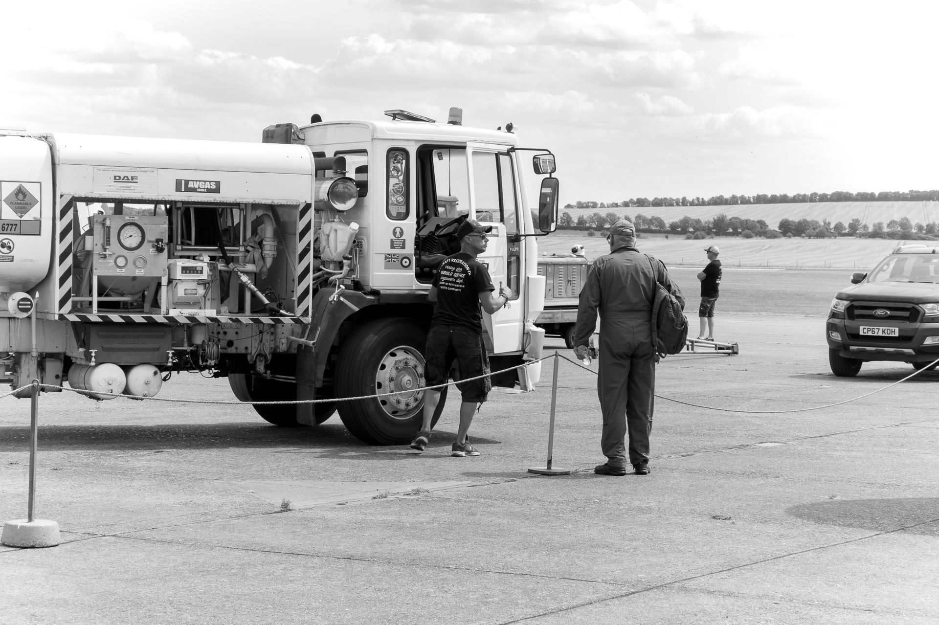 Black and white photo of airport fire truck with ground crew personnel on tarmac near parked vehicles.