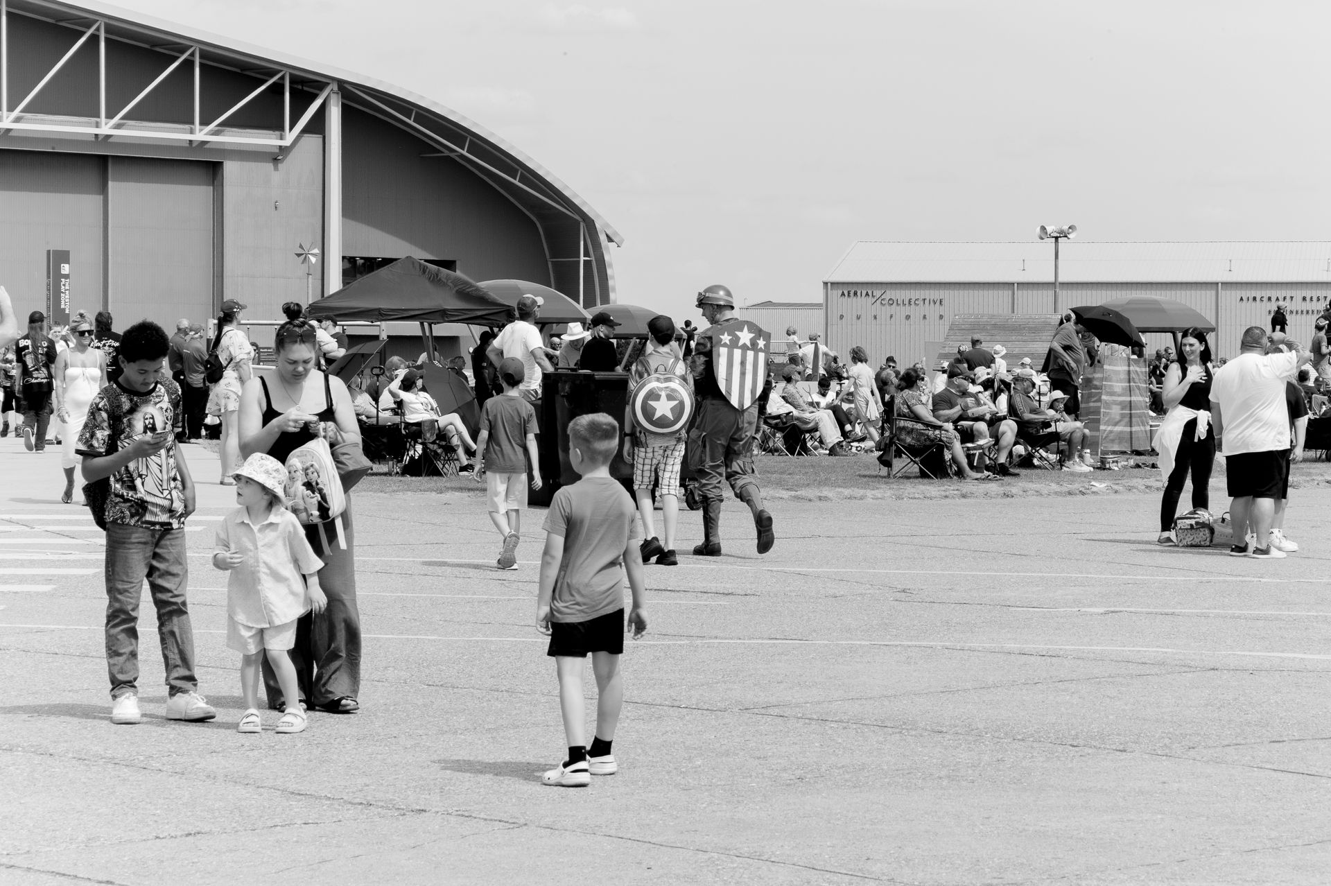 Black and white photo of families and visitors gathered outside a large hangar building at an outdoor airshow event.