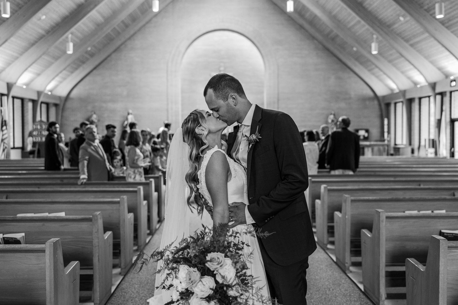 Black and white photo of a bride and groom sharing a kiss at the altar inside a beautiful church.
