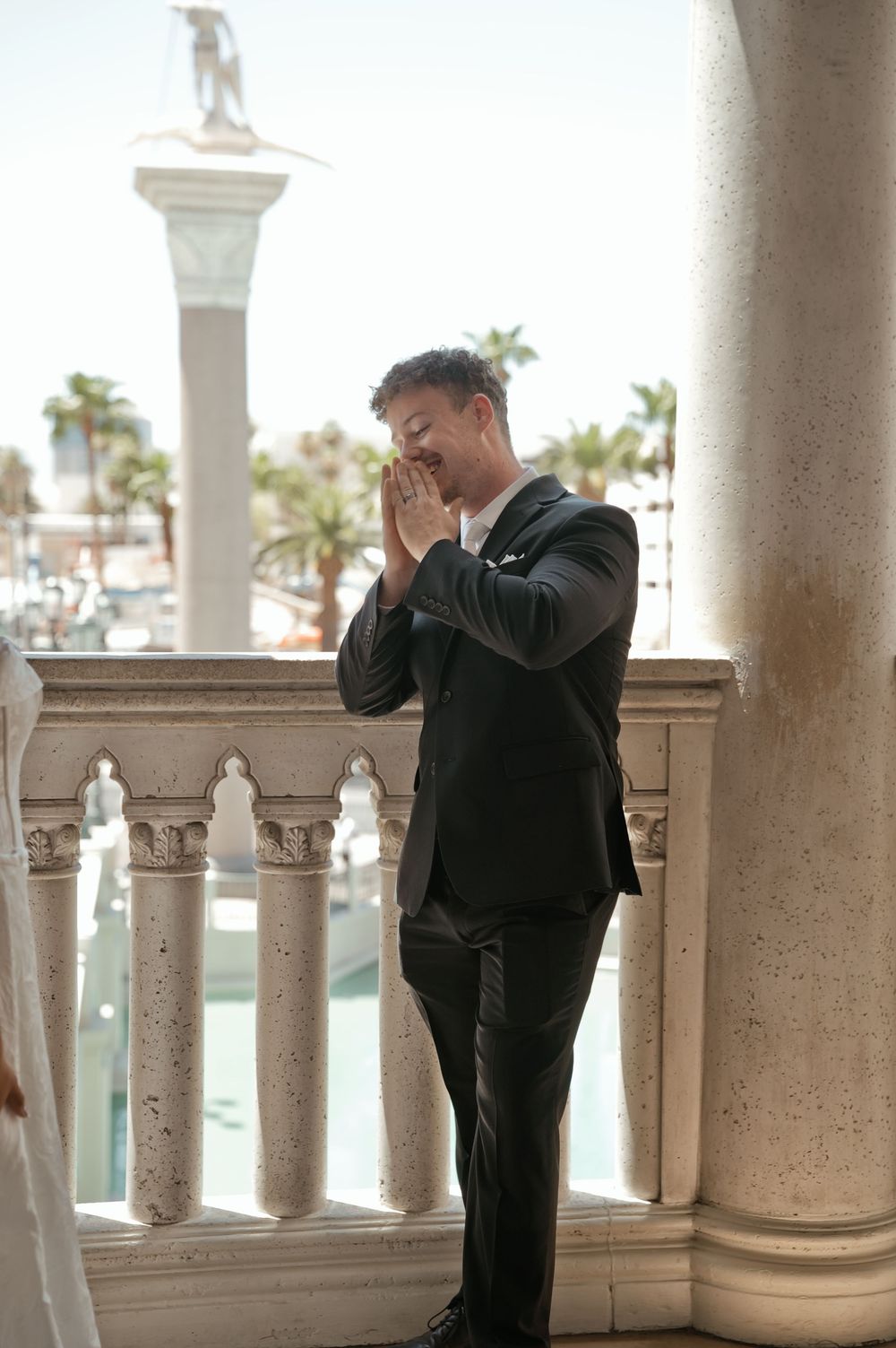 Emotional groom in black suit clasping hands on ornate balcony at The Venetian Las Vegas during wedding ceremony.