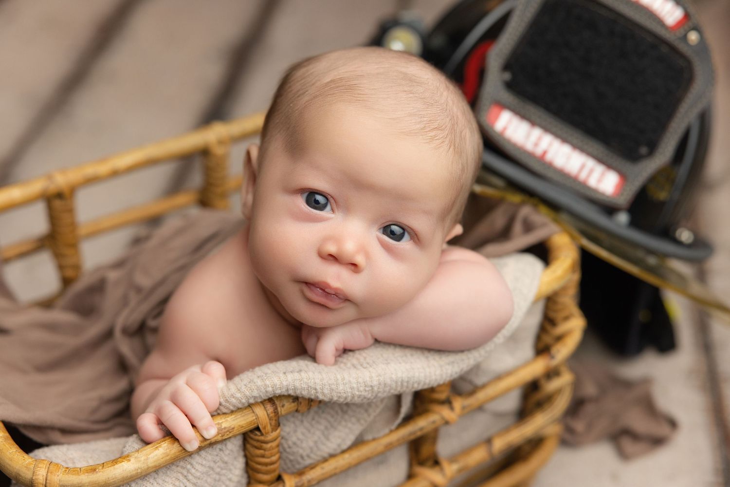 Newborn baby wrapped in teal swaddle holding green knit bear toy, resting in decorative bucket.