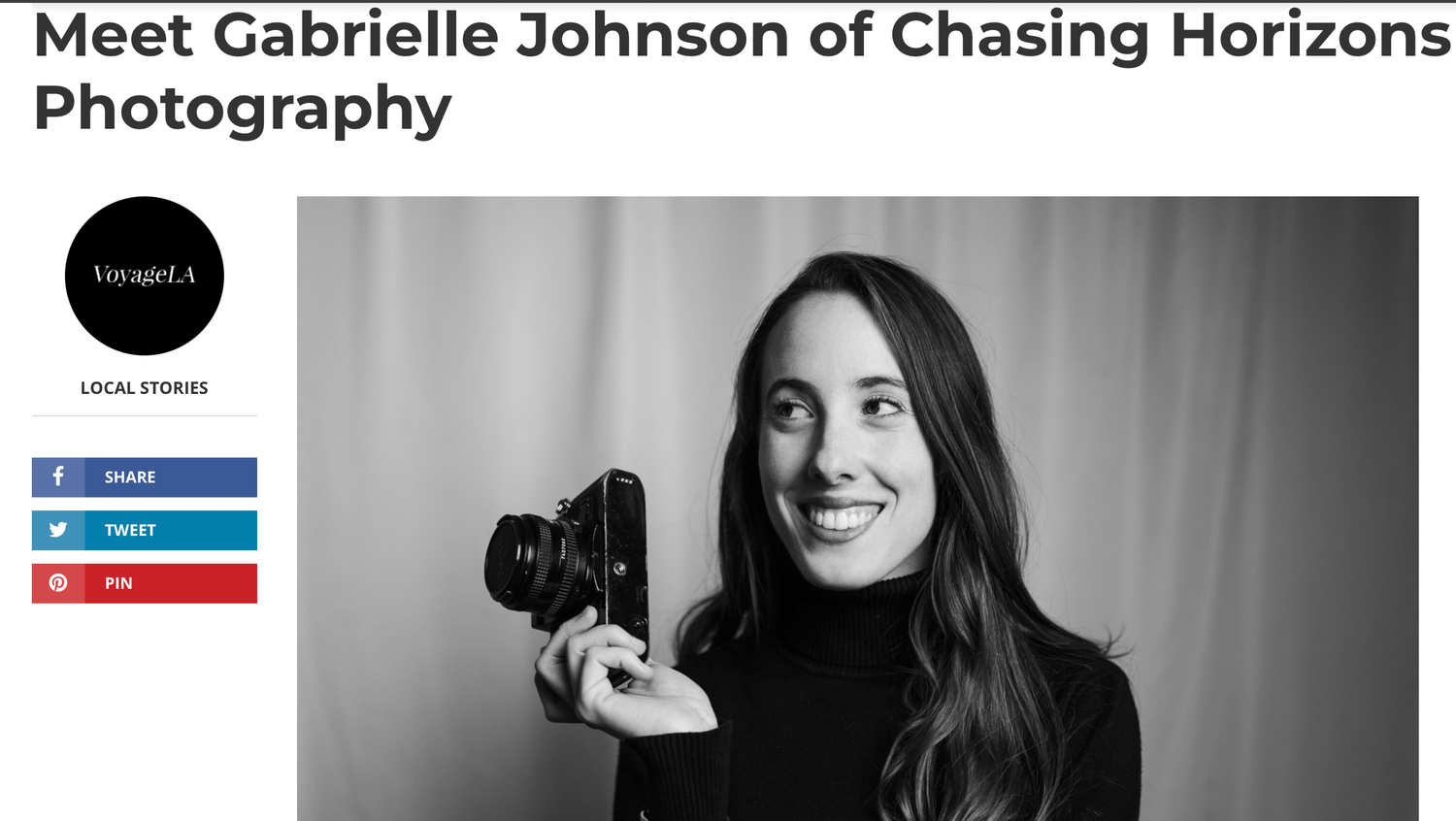 Smiling woman with long dark hair holding a vintage film camera, black and white portrait photo.