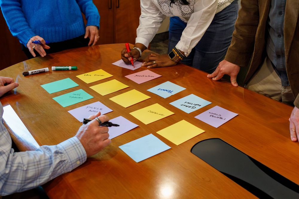 Group brainstorming session with colorful sticky notes on a wooden conference table, participants writing ideas with markers.