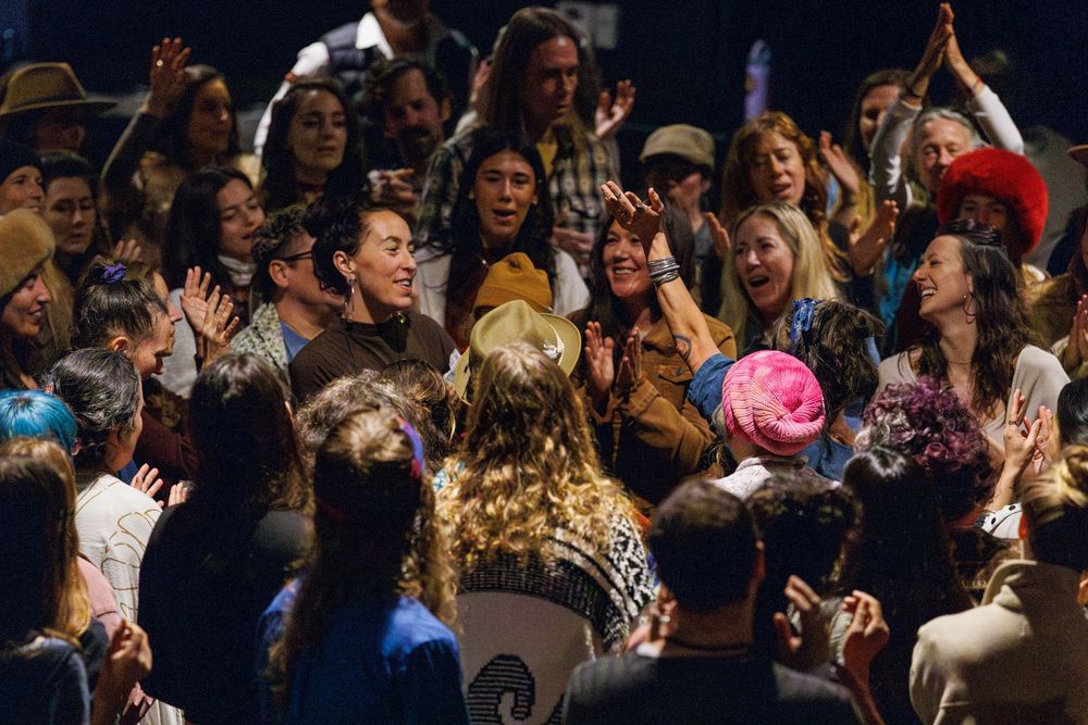 Diverse crowd of people gathered together, smiling and celebrating at an indoor event or concert.