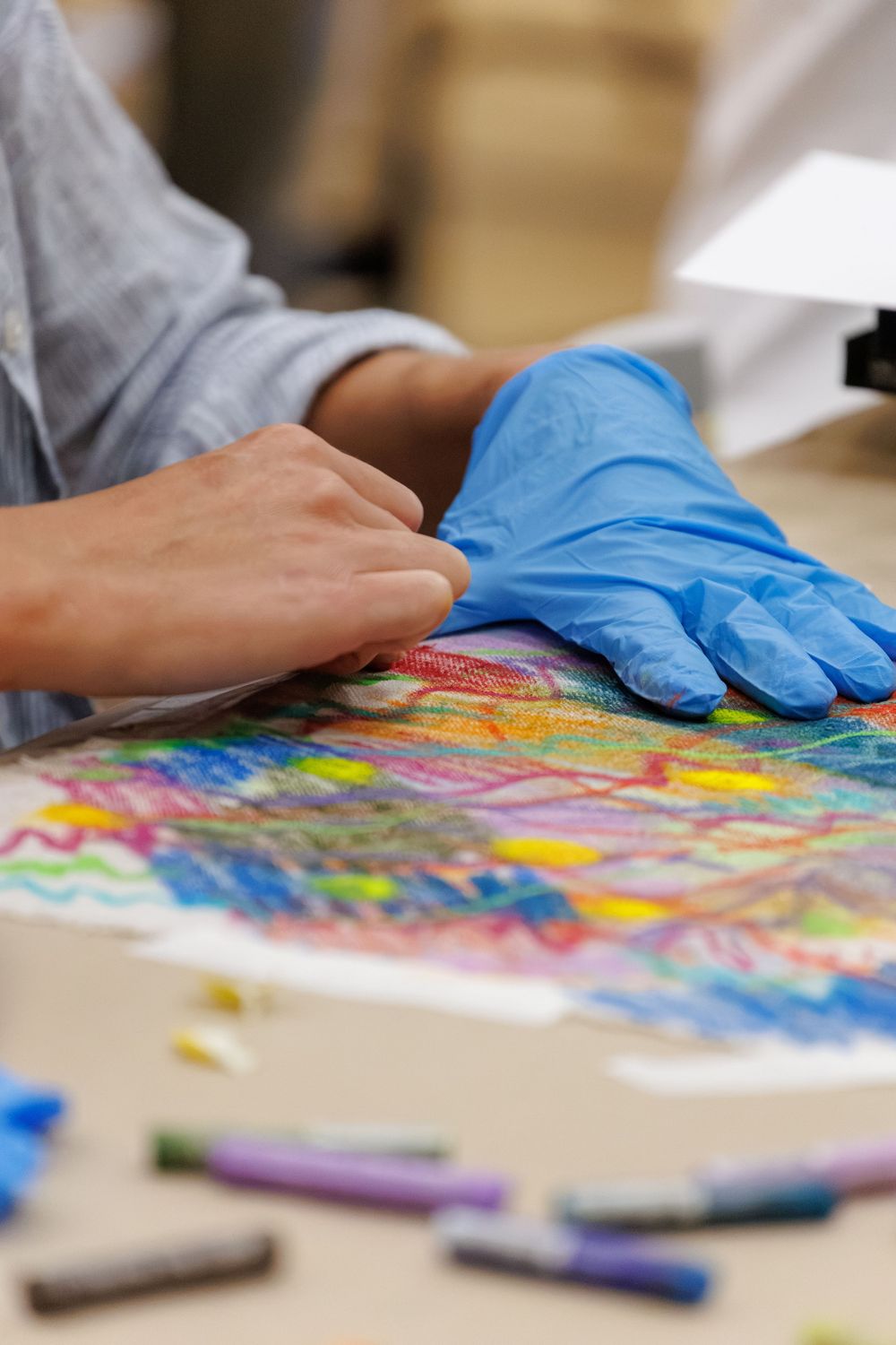 Close-up of hands with blue latex glove on colorful crayon drawing artwork on white paper.