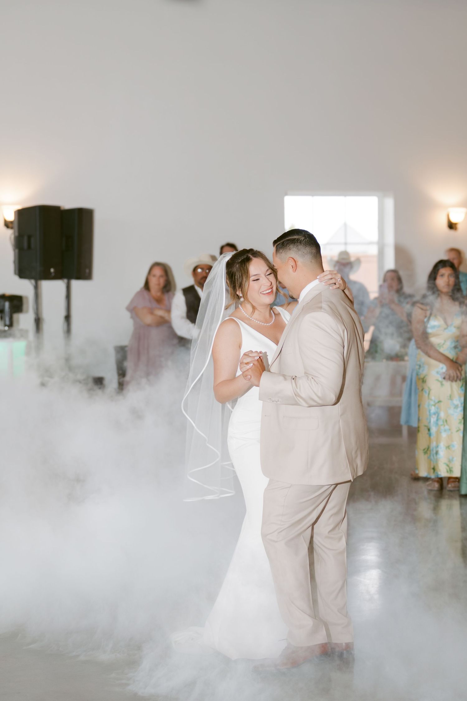 Bride and groom share first dance surrounded by fog machine clouds at elegant wedding reception.