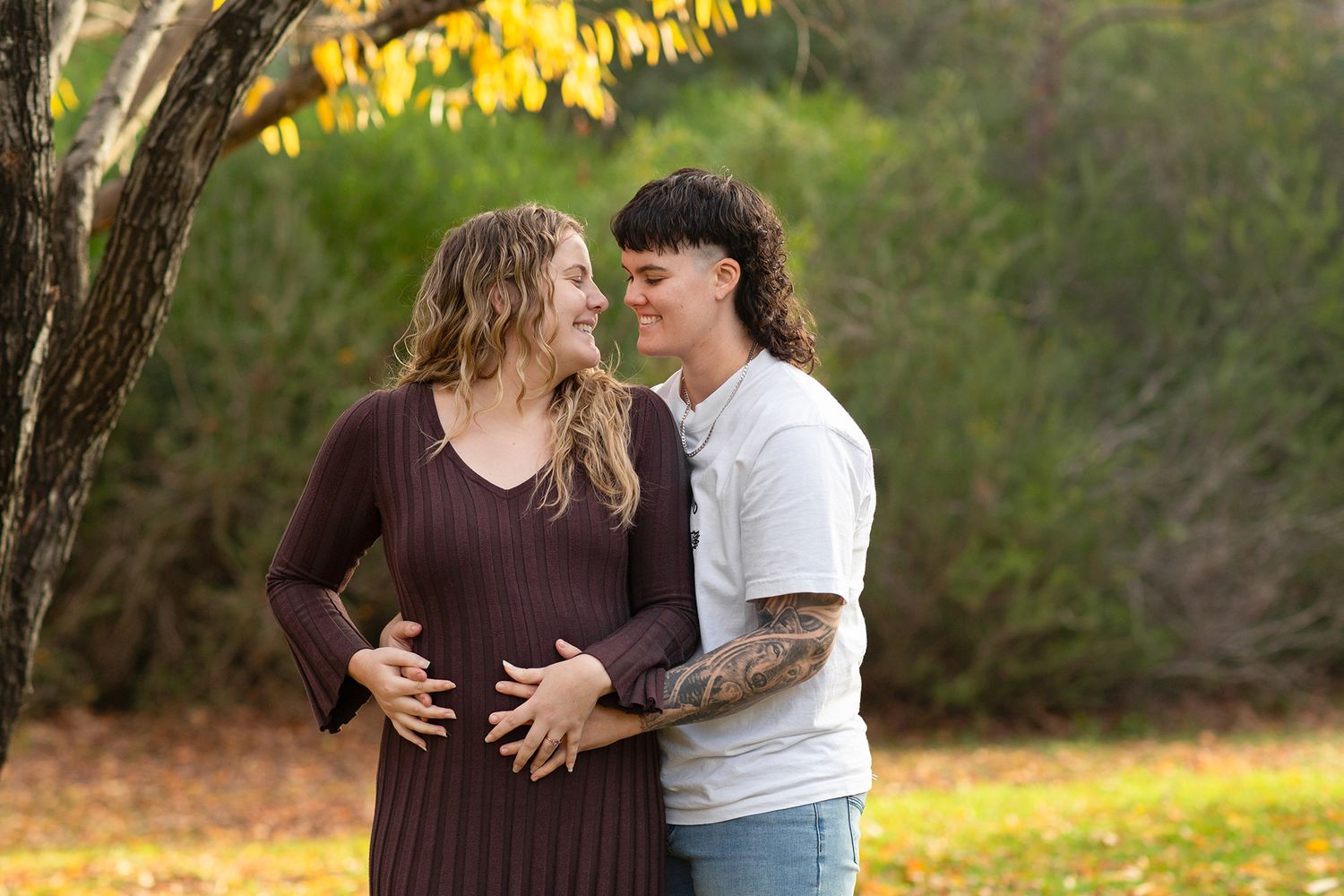 Couple embracing while holding baby bump surrounded by trees during autumn in Perth