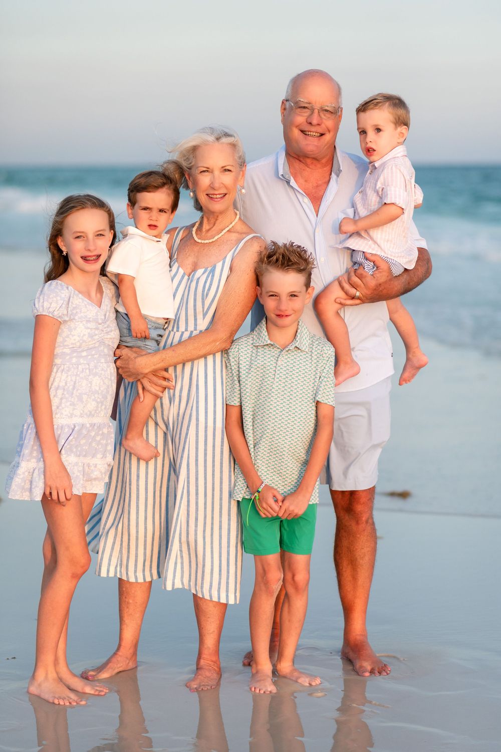 Grandparents with four grandchildren posing together on a sandy beach at sunset.