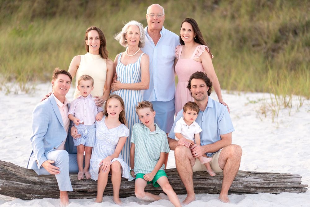Multi-generational family posing together on a sandy beach, smiling in coordinated pastel outfits.