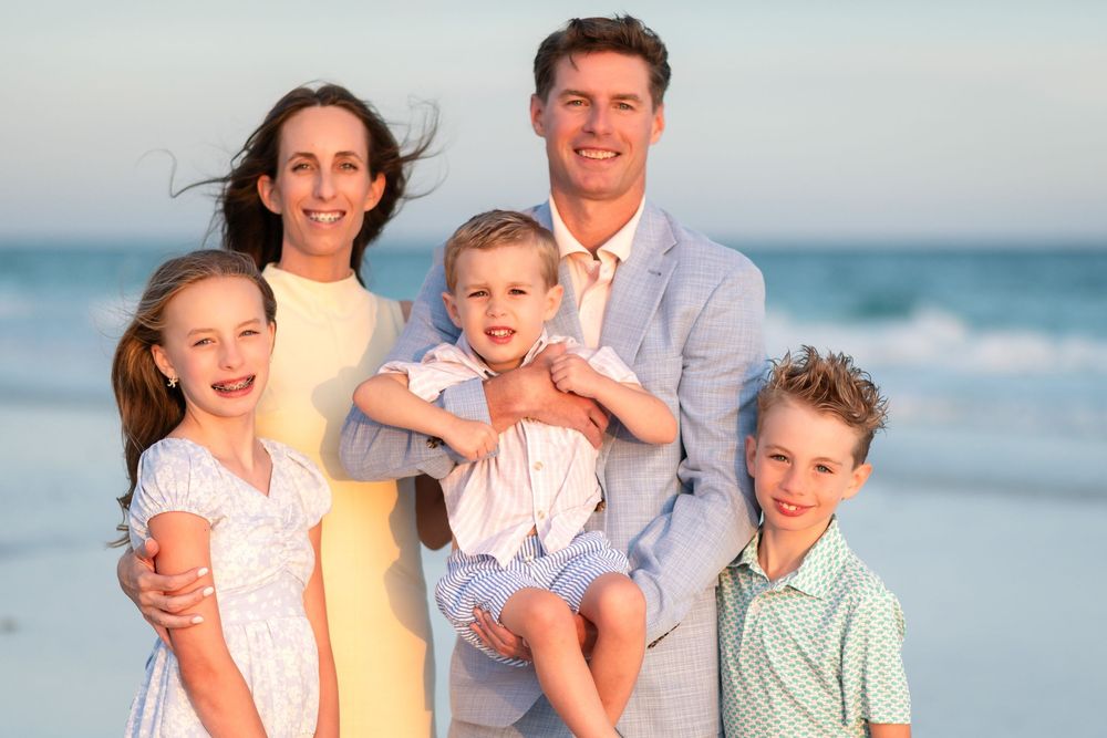 Happy family of five smiling together on a sandy beach at sunset, parents with three young children.
