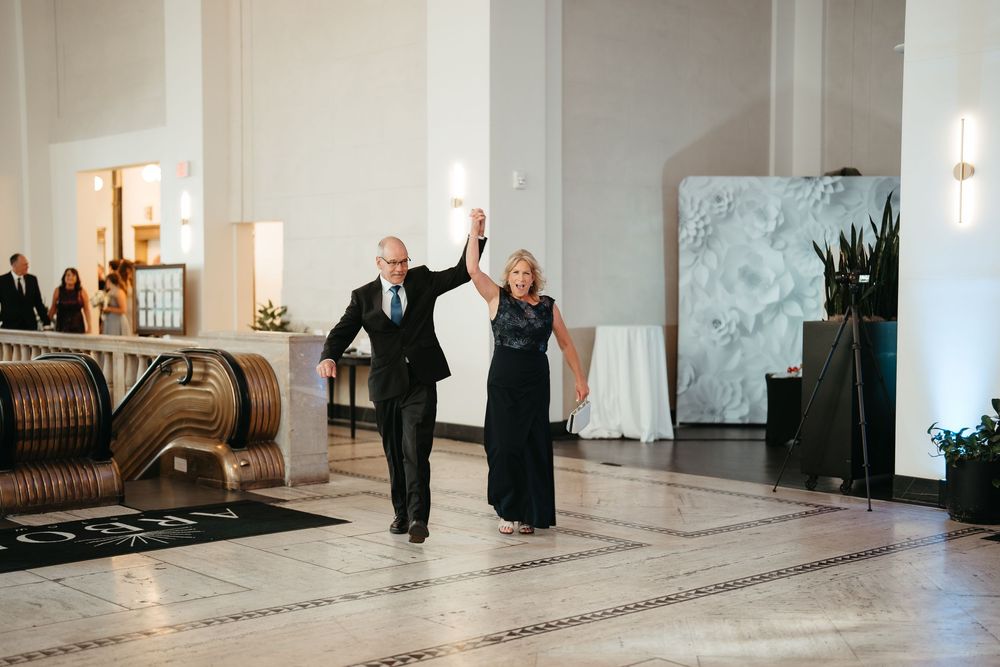 Elegant couple raising hands in grand marble hall during wedding reception entrance at upscale venue.