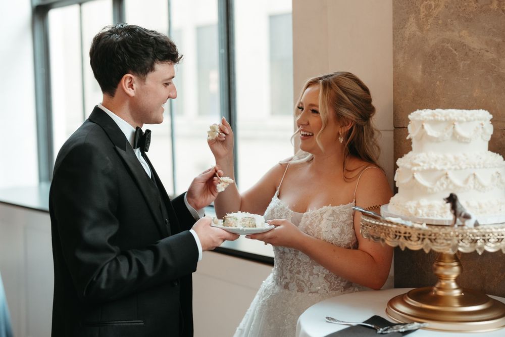 Bride and groom smiling while feeding each other wedding cake at their elegant reception.