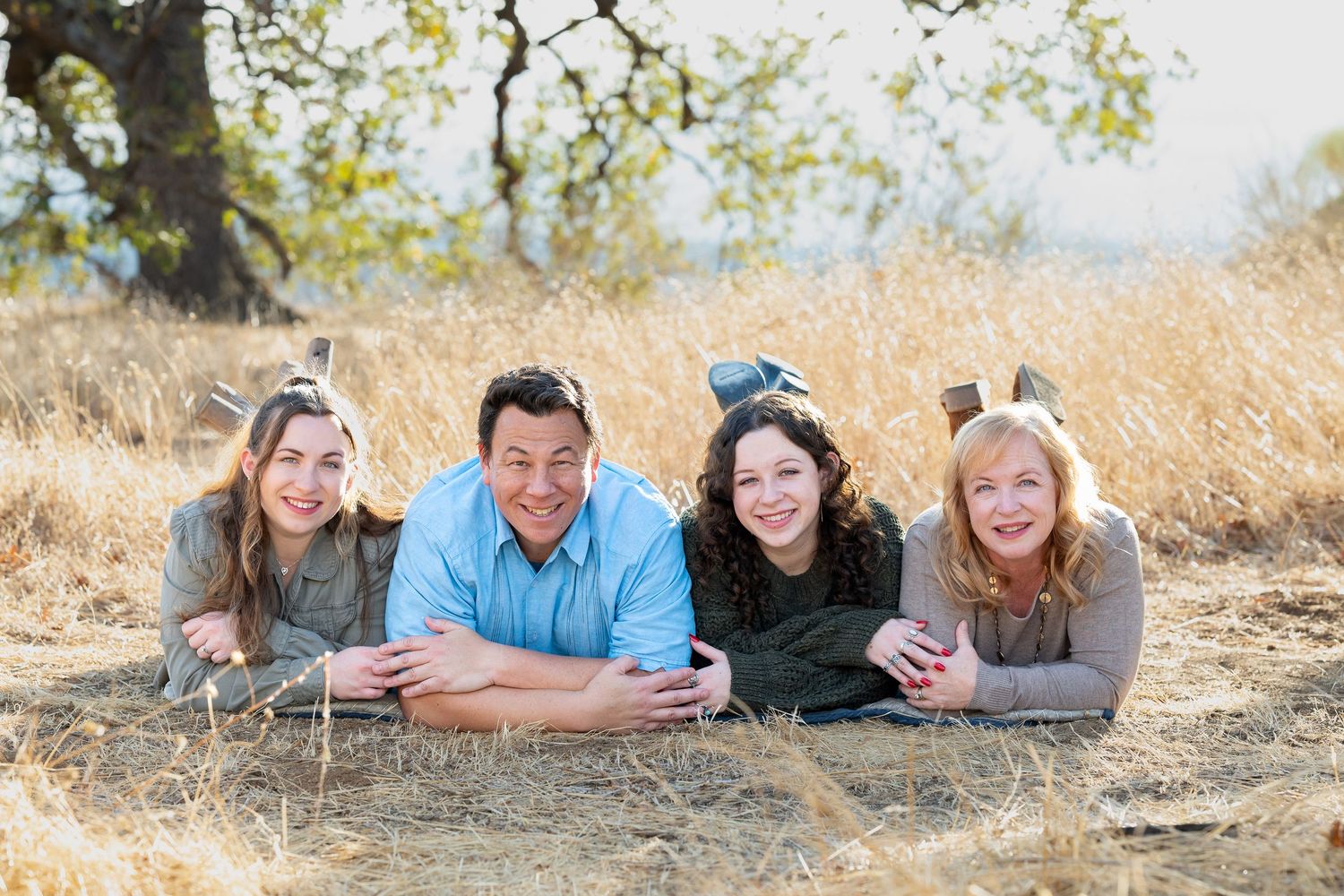 Large multigenerational family posing outdoors in coordinating blue shirts and jeans under a sprawling tree.