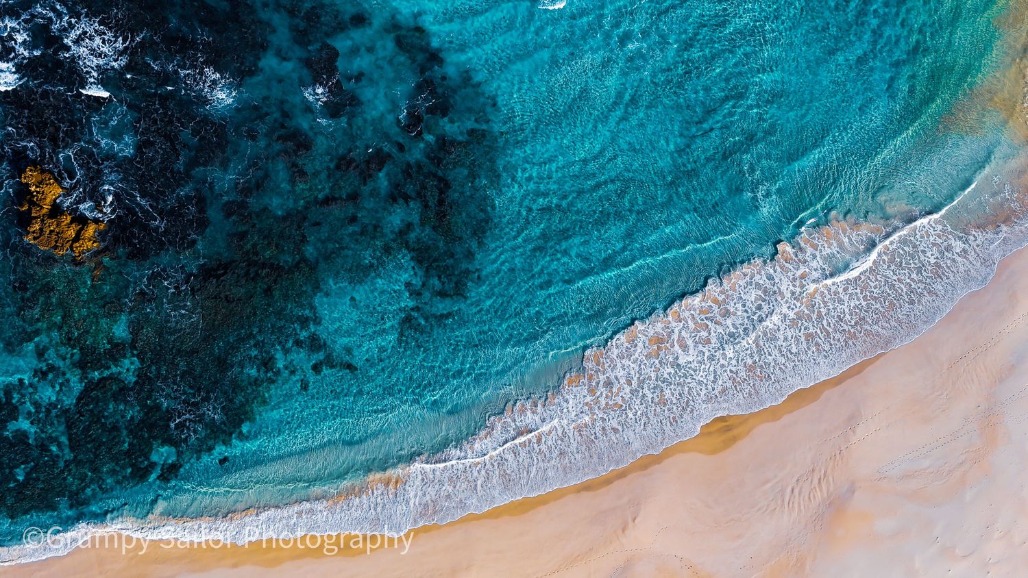 Aerial drone shot of vivid turquoise waves washing onto sandy shore.