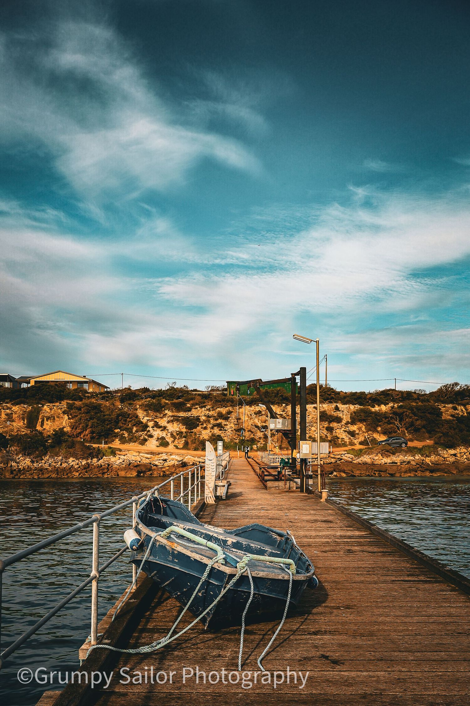 Weathered wooden jetty with an old blue boat moored alongside under dramatic cloudy sky at golden hour.
