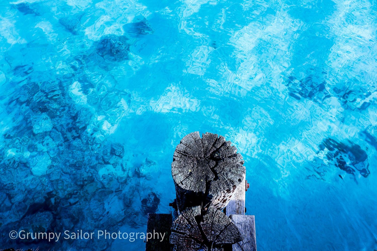 Top-down view of weathered wooden pier post over crystal clear bright blue ocean water.