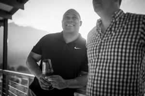 Two men laughing and sharing drinks on an outdoor deck in a black and white photo.