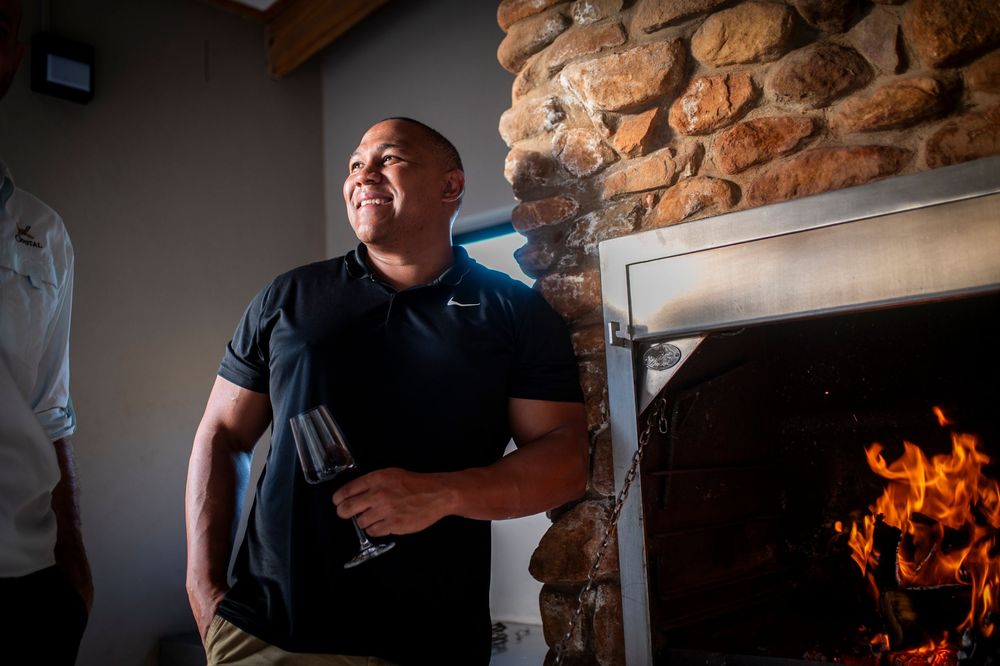 Man holding wine glass smiling by stone fireplace indoors.