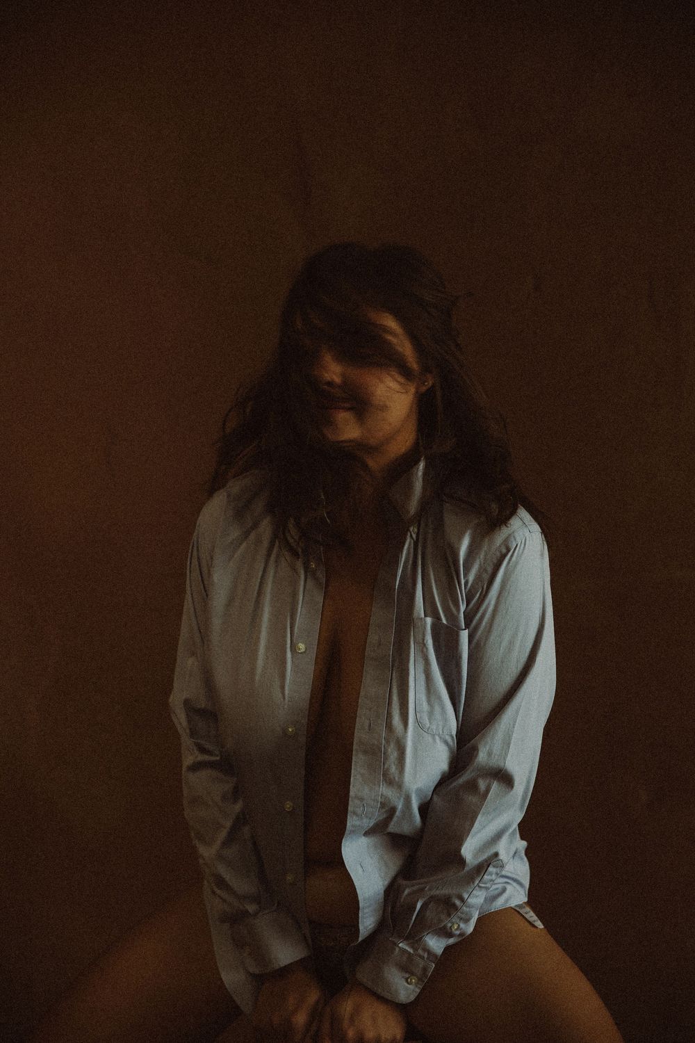 Woman in an open white shirt smiling with hair blowing across her face in warm light.