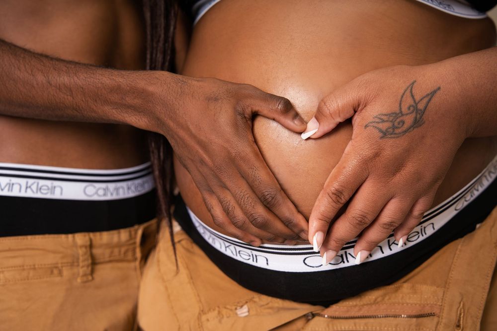 Couple forming heart shape with hands on pregnant belly wearing matching Calvin Klein underwear.