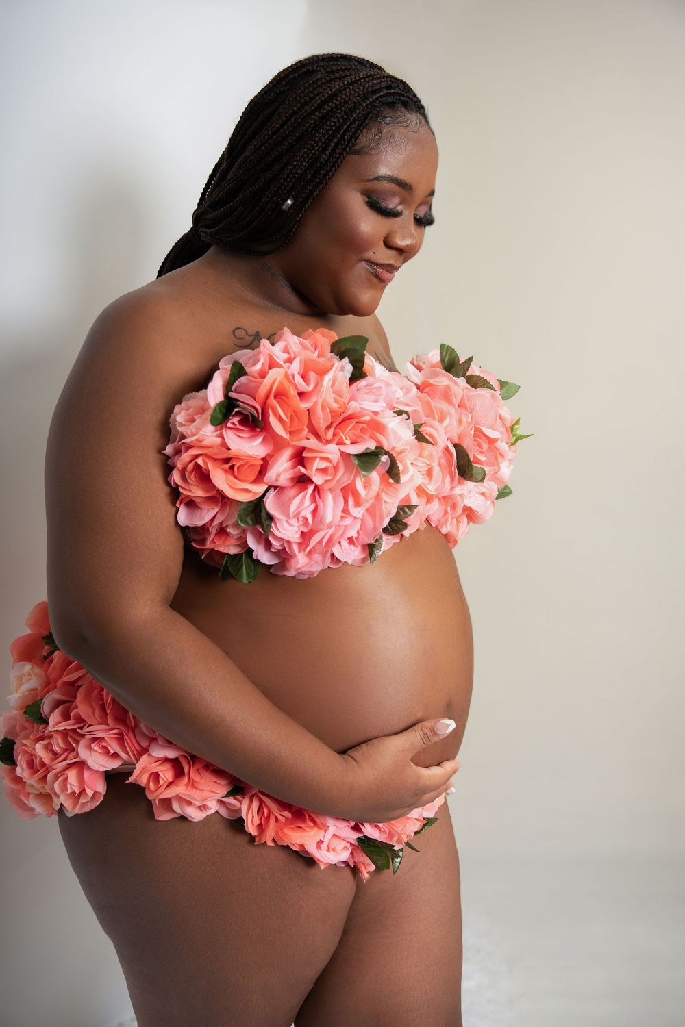 Pregnant woman posing with pink roses covering her chest and hips, smiling downward at her belly.