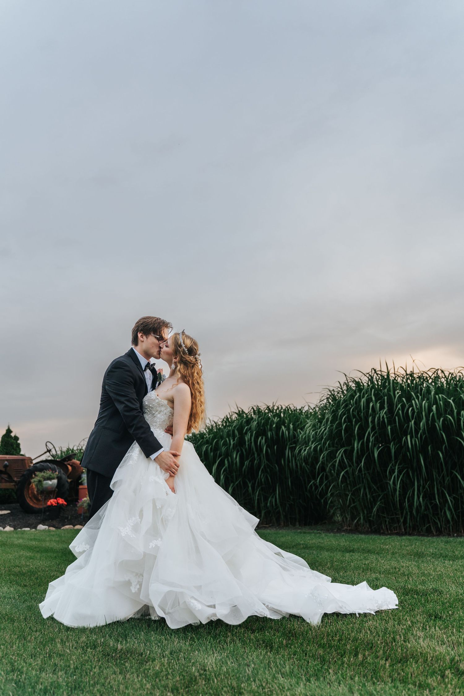 A romantic wedding couple shares a dip kiss under a large tree with long flowing white dress and veil for their photos.