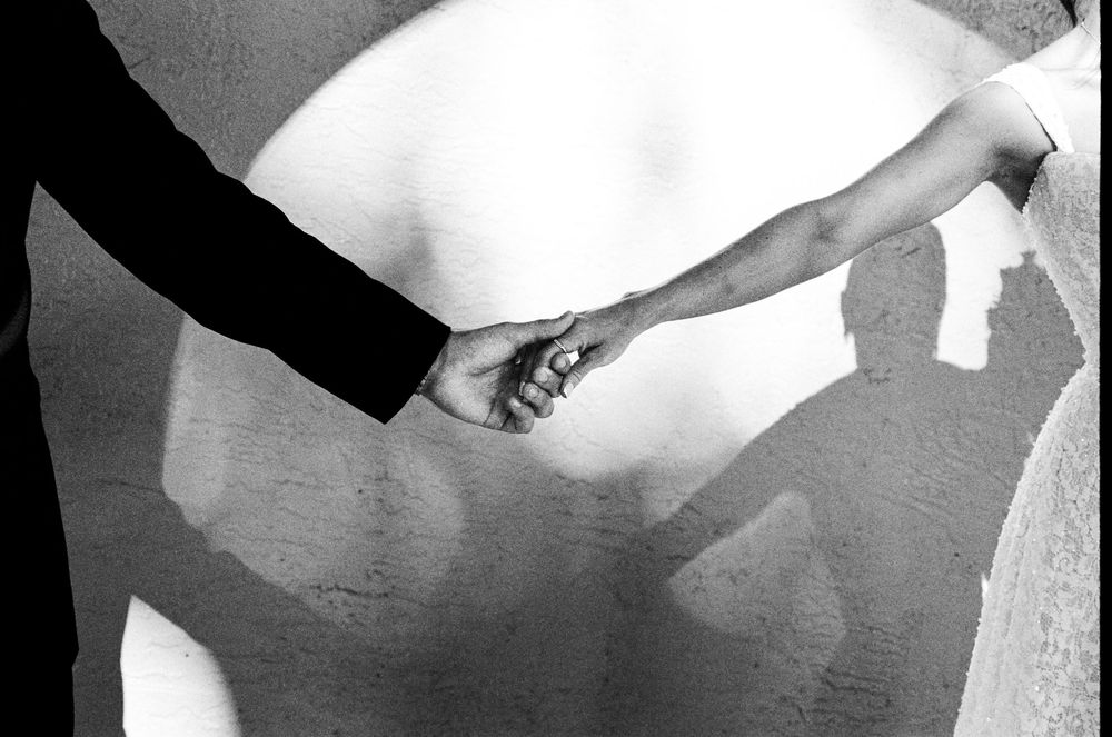 Black and white photo of a bride and groom holding hands, casting romantic shadows on a wall.