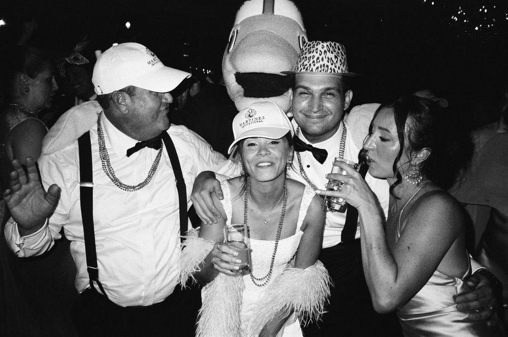 Black and white photo of four friends in festive costumes celebrating at a party, holding drinks and smiling.