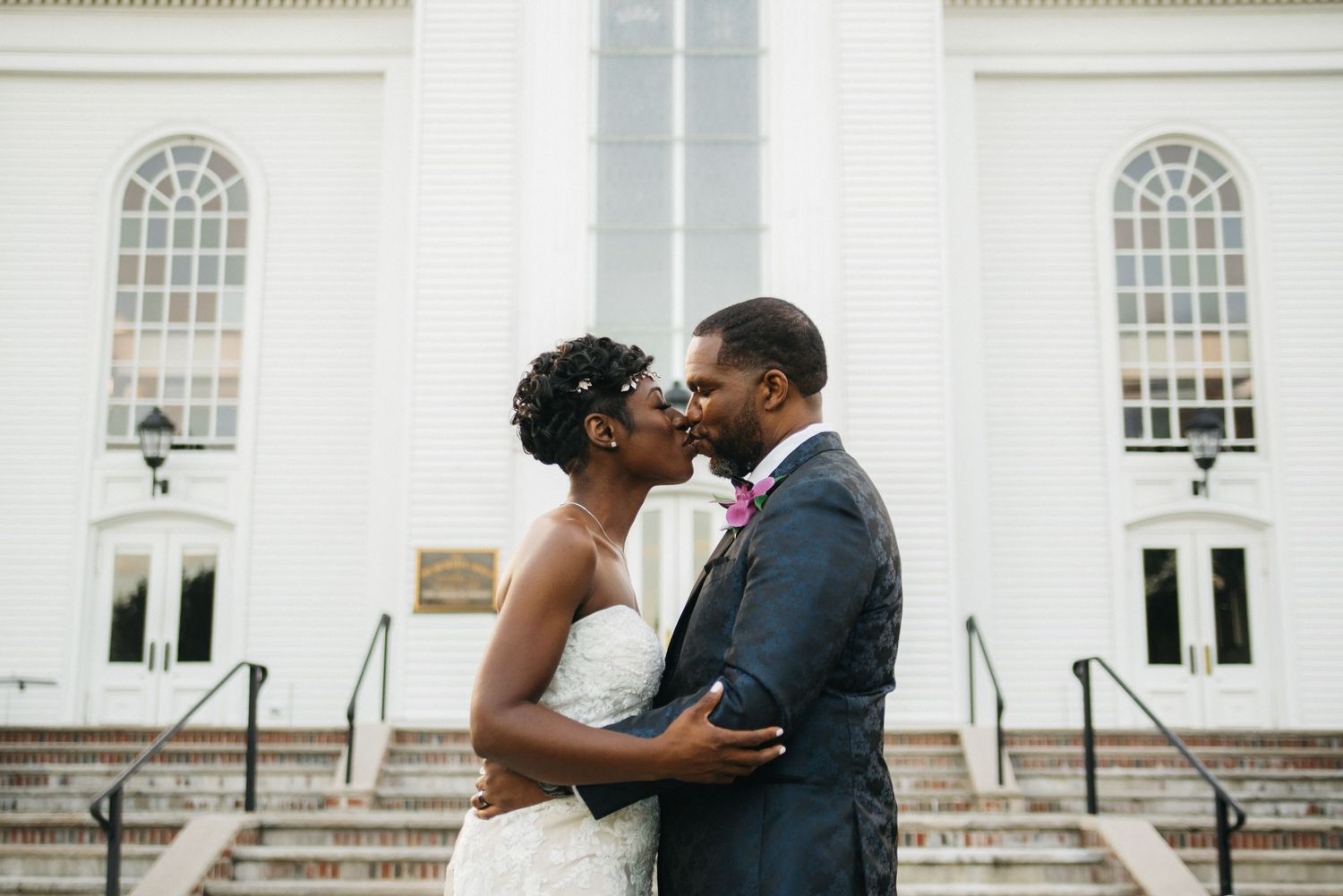 Black and white wedding photo of smiling bride in lace gown with drop earrings embracing groom in tender moment.