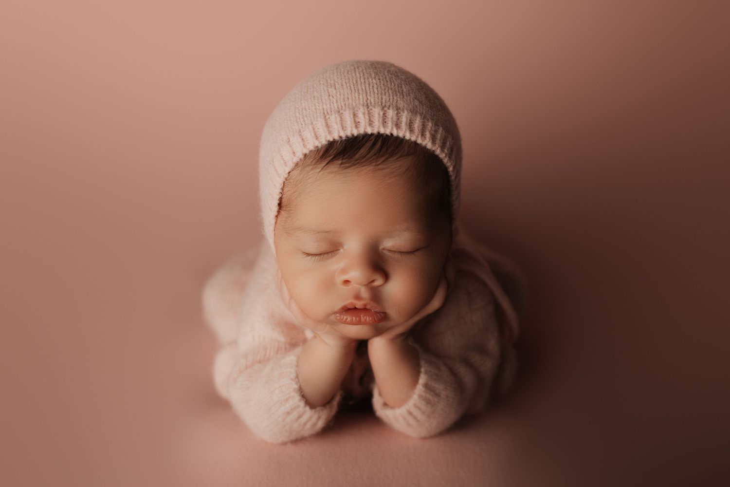 Newborn baby swaddled in gray wrap sleeping peacefully on a small wooden bed with a white pillow.