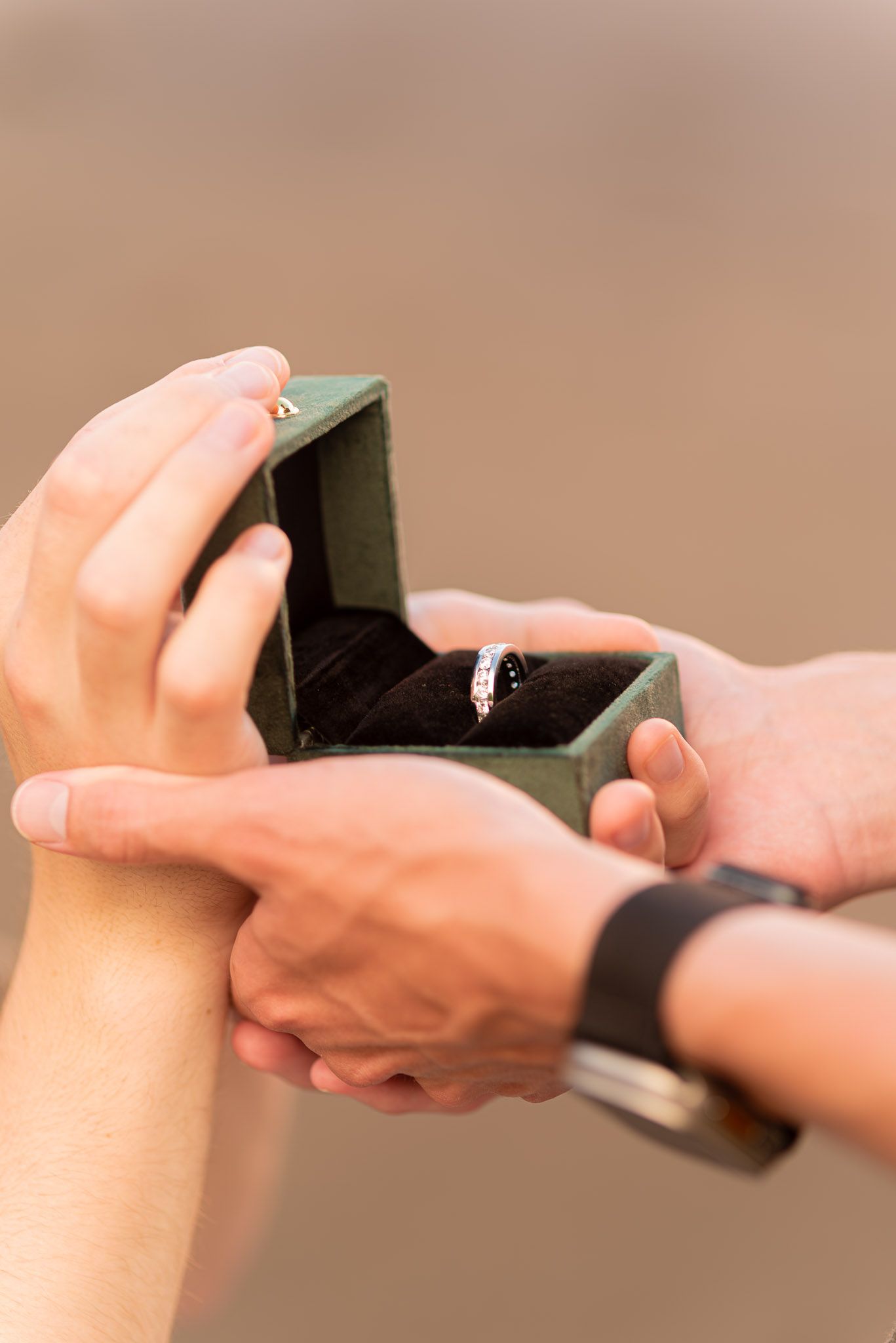Hands holding an open green ring box with a diamond engagement ring inside during a marriage proposal.